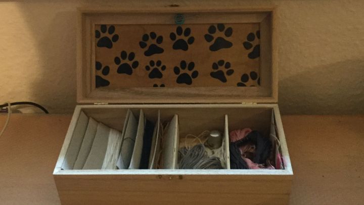 Eine Holzbox f&uuml;r Teebeutel steht ge&ouml;ffnet auf einem Tisch, zeigt Innenf&auml;cher und ein Pfotenmuster im Deckel.