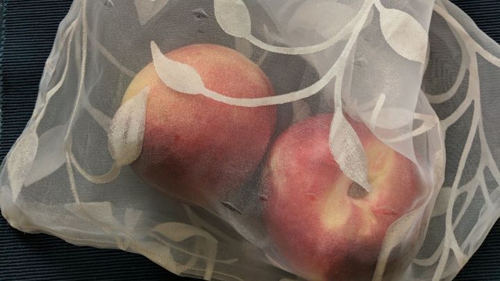 Ein netzartiger Beutel aus Gardinen-Resten h&auml;lt mehrere &Auml;pfel und liegt auf einem blauen Untergrund.