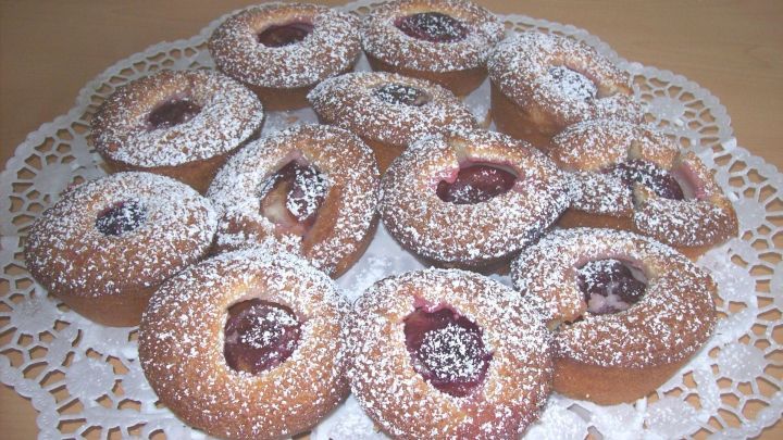 Saftige Pflaumen-Muffins mit Marzipan liegen auf einer dekorativen Serviette, mit Puderzucker best&auml;ubt.