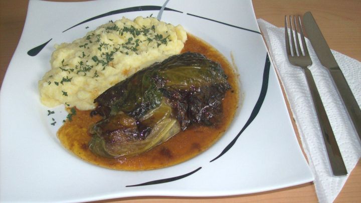 Rostbratwurst umh&uuml;llt von Wirsing, serviert mit cremigem Kartoffelbrei auf einem eleganten wei&szlig;en Teller.