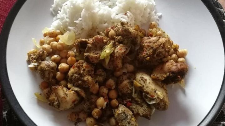 Ein Teller mit marokkanischem Huhn und Kichererbsen wird serviert, begleitet von einer Portion Reis.