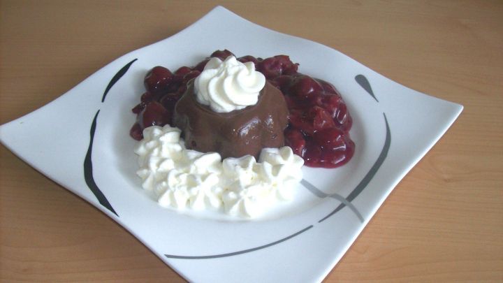 Ein Schokopudding liegt in der Mitte eines eleganten Tellers, umgeben von Kirschkompott und Sahne.