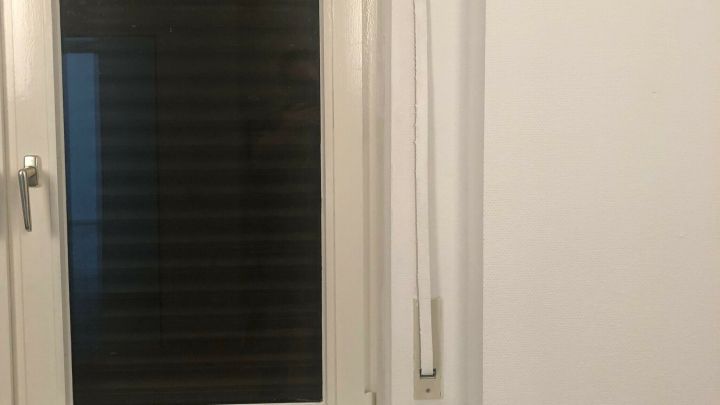 Ein Rolladengurt h&auml;ngt neben einem geschlossenen Fenster, bereit f&uuml;r die Auffrischung in einem modernen Raum.