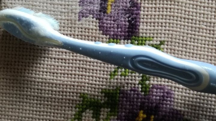 Ein Stickbild mit lila Bl&uuml;ten wird mit einer Zahnb&uuml;rste gereinigt, um das alte Stickbild aufzufrischen.