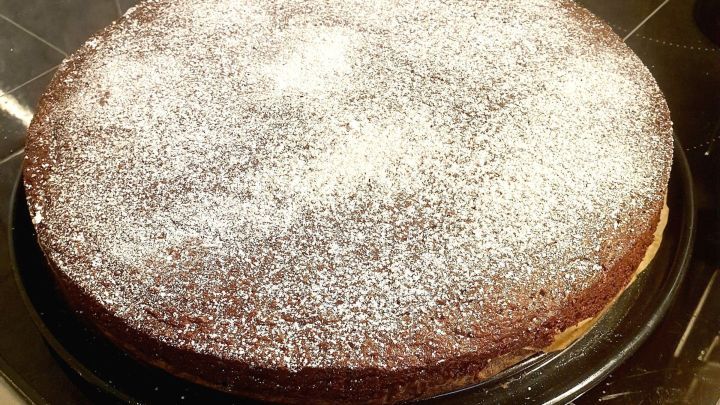 Ein k&ouml;stlicher Schokoladenkuchen liegt auf einer schwarzen Platte und ist mit Puderzucker best&auml;ubt.