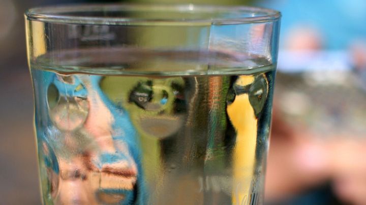 Ein Glas Wasser steht auf einem Tisch, reflektiert Licht und zeigt eine unscharfe Umgebung mit verschwommenen Farben.