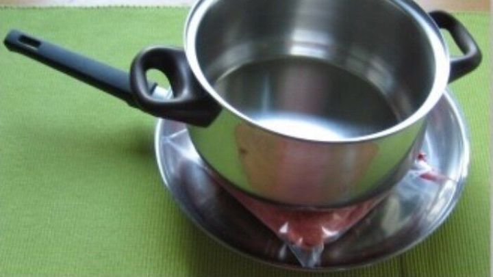 Ein Topf mit Wasser steht auf einem Teller, w&auml;hrend er schonend Lebensmittel taut. Der Hintergrund ist hellgr&uuml;n.