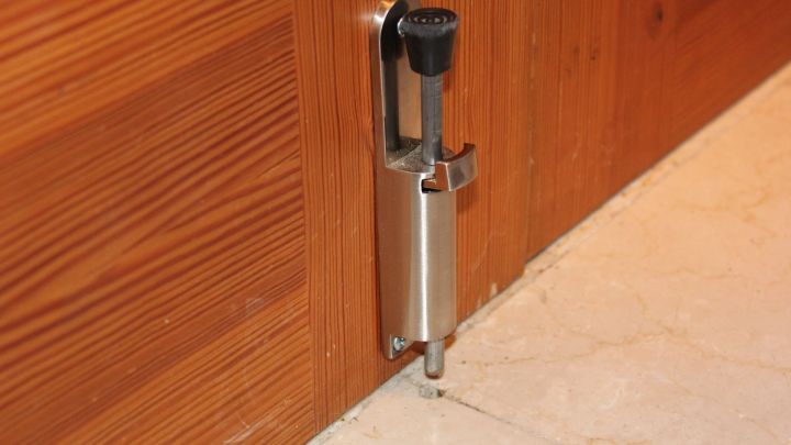 Ein stabiler T&uuml;rstopper aus Metall steht an einer h&ouml;lzernen Eingangst&uuml;r und sichert diese gegen Einbr&uuml;che.