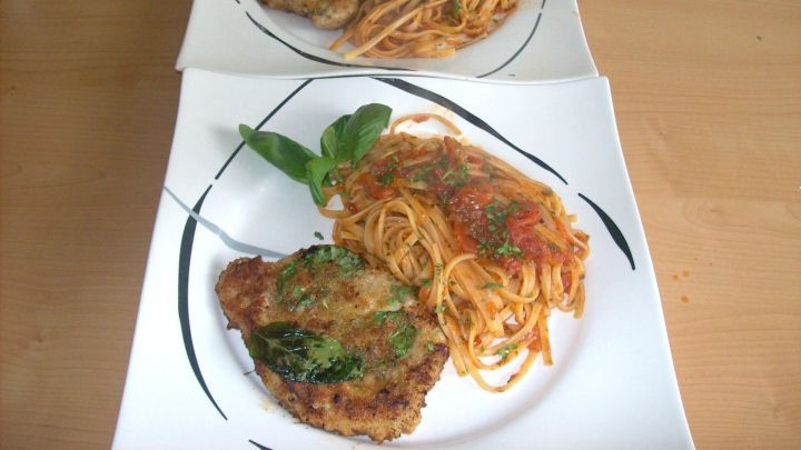 Ein knuspriges Schnitzel vom Schwein alla Milanese liegt auf einem Teller und wird mit Spaghetti in Tomatensauce serviert.