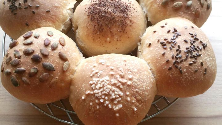 Zehn frisch gebackene Br&ouml;tchen stehen in Form einer Blume auf einem Kuchengitter. Sie haben verschiedene Toppings.