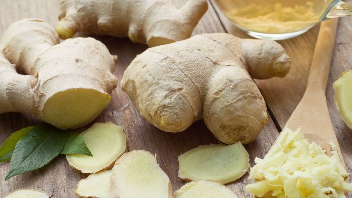 Frischer Ingwer liegt auf einem Holzbrett, w&auml;hrend daneben Ingwerscheiben und eine Tasse Ingwertee stehen.