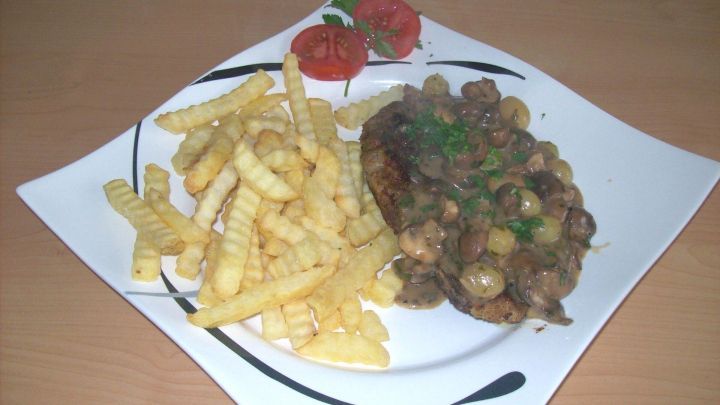 Ein krosses Winzer-Kotelett liegt auf einem Teller, garniert mit einer Pilzsauce, daneben liegen knusprige Pommes.