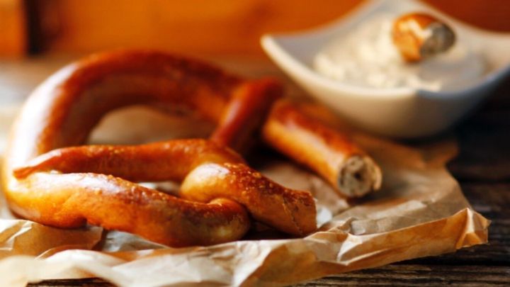 Krosse Laugenbrezeln liegen auf braunem Papier und begleiten eine kleine Schale mit cremigem Dipp auf einem Holztisch.