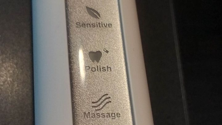 Ein elektrisches Ger&auml;t mit Tasten zur Nutzung von Ultraschall und verschiedenen Reinigungsmodi liegt auf einer Oberfl&auml;che.