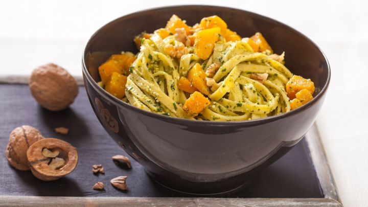 Eine Sch&uuml;ssel Bandnudeln mit K&uuml;rbis, Maronen und Thymian ist gef&uuml;llt mit buntem Gem&uuml;se und serviert auf einem Holzbrett.