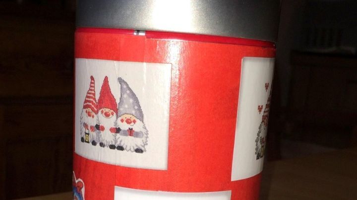 Eine rote Weihnachtskeksdose steht auf einem Holztisch, dekoriert mit fr&ouml;hlichen Weihnachtsm&auml;nnern und Schneeflocken.