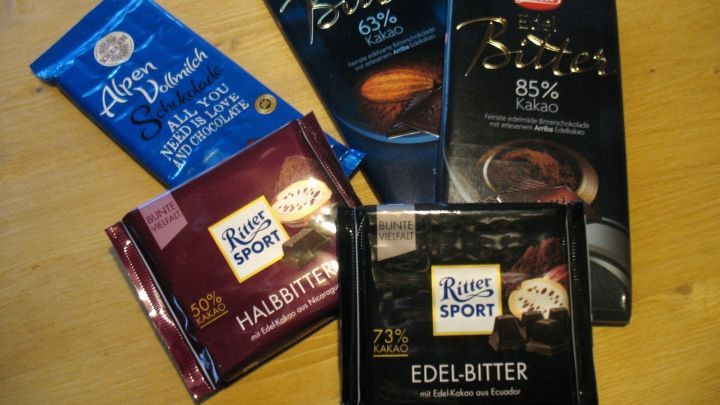 Dunkle Schokoladenverpackungen liegen auf einem Holzuntergrund und zeigen verschiedene Sorten mit unterschiedlichen Kakaoanteilen.