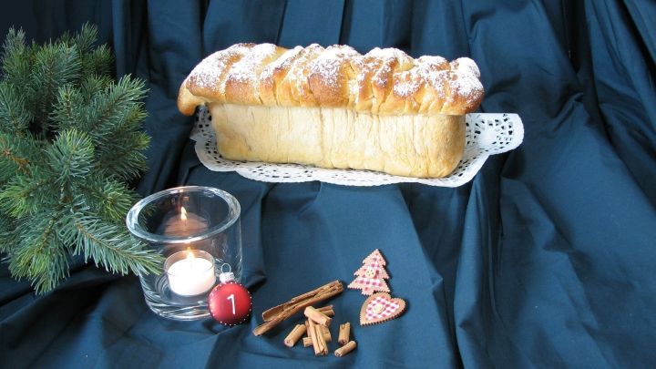 Ein frisch gebackenes Bratapfelzupfbrot liegt auf einer wei&szlig;en Podestplatte, umgeben von weihnachtlichen Dekorationen und einer Kerze.