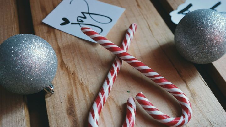 Zwei silberne Weihnachtskugeln und zuckerhaltige Candycanes liegen auf einem Holzbrett, umgeben von festlicher Dekoration.