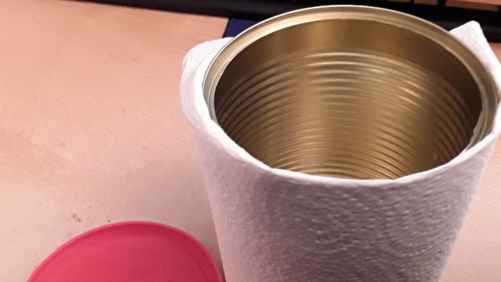 Ein Beh&auml;lter aus Metall mit einem roten Deckel liegt neben einer wei&szlig;en Fassung; geeignet zur sicheren Entsorgung von Bratfett.