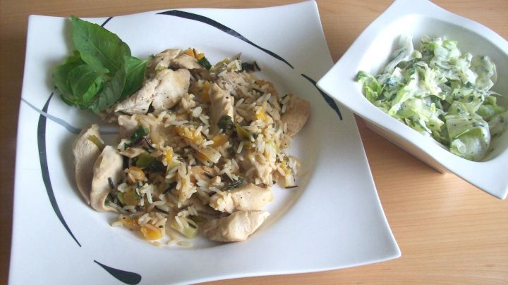 Auf einem wei&szlig;en Teller liegt eine Wildreispfanne mit zarten H&auml;hnchenfiletstreifen, daneben ein frischer Salat.