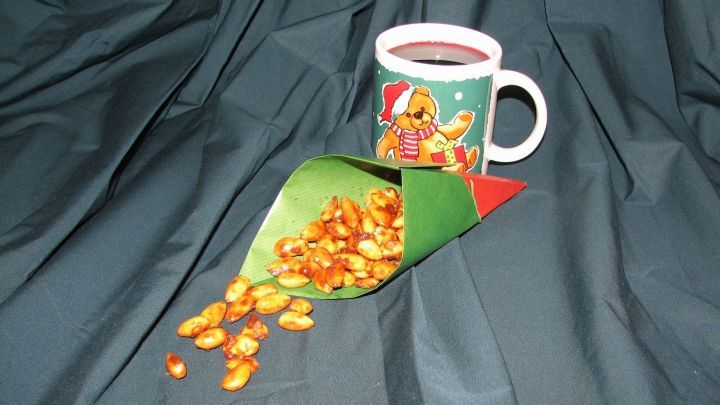 Eine Tasse mit hei&szlig;em Muskatkaffee steht neben einer gr&uuml;nen Papiert&uuml;te, aus der gebrannte Mandeln fallen.