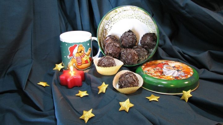 Rumkugeln sind in einer dekorativen Schale arrangiert, umgeben von glitzernden Sternen und einem Weihnachtsbecher.