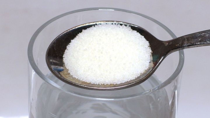 Ein L&ouml;ffel mit wei&szlig;em Zuckerkristallen schwebt &uuml;ber einem Glas Wasser und k&ouml;nnte als Hausmittel gegen entz&uuml;ndetes Zahnfleisch dienen.