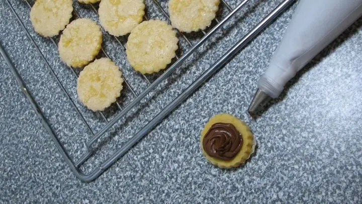 Jeweils 1 Plätzchen nehmen, Füllung aufdressieren und mit einem zweiten Orangentaler zudecken – sehr leicht andrücken.