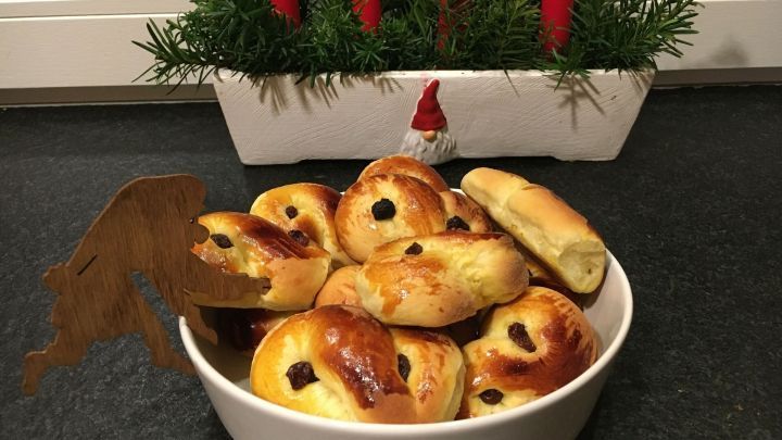 Lussekatter liegen in einer Sch&uuml;ssel, umgeben von Tannenzweigen und roten Kerzen, als festliche Leckerei.