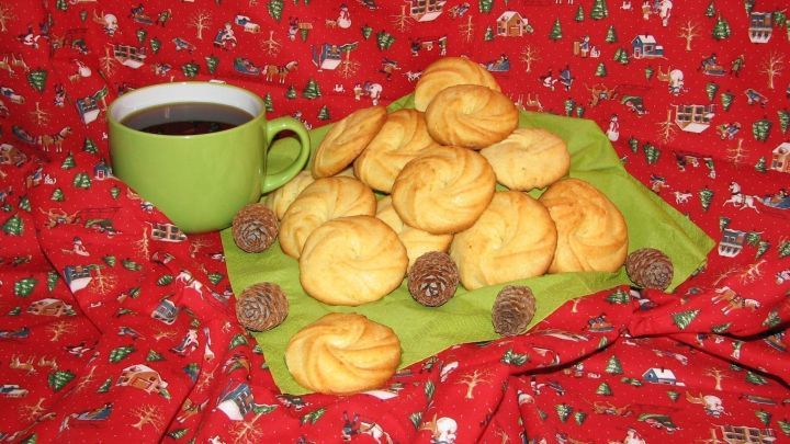 Kekse liegen auf einem gr&uuml;nen Teller, w&auml;hrend eine Tasse schwarzer Kardamom-Kaffee daneben steht, vor rotem Tischcloth.