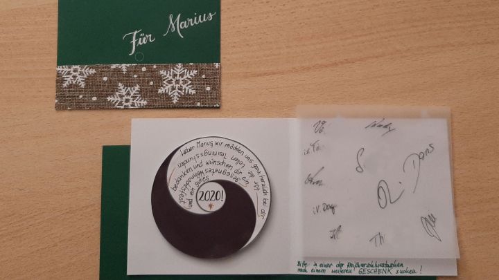 Eine gr&uuml;ne Weihnachtskarte mit Yin und Yang Symbol liegt offen auf einem Holztisch, umgeben von einer gr&uuml;nen Umschlagklappe.