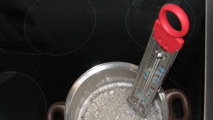 Sobald sich der Zucker aufgelöst hat und der Sirup klar ist, das Zuckerthermometer einhängen. Dieses hat eine höhenverstellbare Klammer, mit der das Thermometer am Topfrand befestigt werden kann.