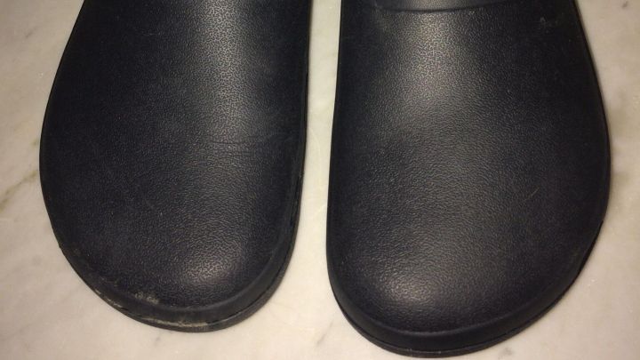 Schwarze Crocs stehen auf einer fensterlosen, hellen Fl&auml;che. Sie wirken robust und bequem, ideal zur Vermeidung von Druckstellen.