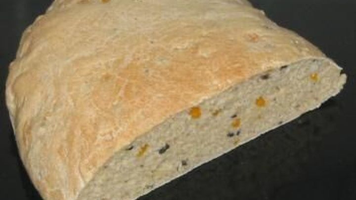 Ein halbes Fladenbrot aus Dinkel mit Paprika- und Olivenst&uuml;cken liegt auf einem schwarzen Tablett.