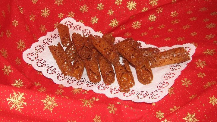 Goldbraune Karamellr&ouml;llchen liegen auf einer dekorativen Servierplatte vor einem festlichen, roten Hintergrund mit Sternen.