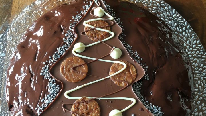 Eine festliche Schokotorte in Form eines Weihnachtsbaums ist mit Glitzer, Schokolade und Dekorationen verziert.