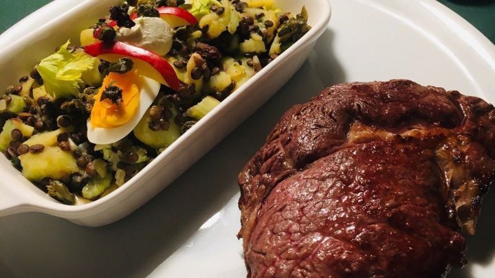 Saftiges Entrecôte liegt neben einem bunten Spezialkartoffelsalat auf einem weißen Teller, umgeben von festlicher Dekoration.