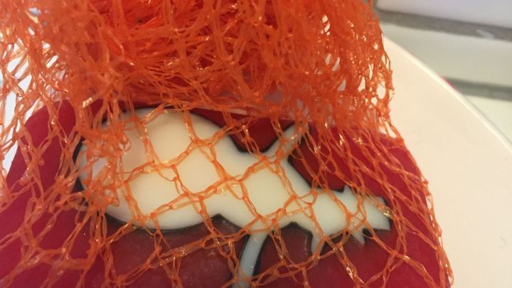 Eine orangefarbene Netzverpackung umschlie&szlig;t eine Seife, die auf einer roten Unterlage liegt, in einem Badezimmer.