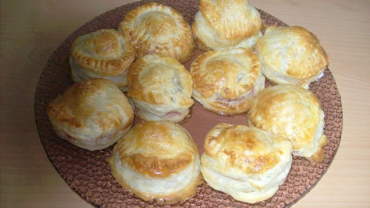 Kleine Bl&auml;tterteigkekse mit goldbrauner Kruste liegen auf einem runden Teller, ideal zum Genie&szlig;en mit Kirschf&uuml;llung.