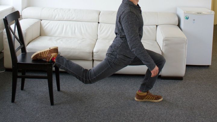 Ein Mann f&uuml;hrt eine Stuhl&uuml;bung aus, indem er einen Ausfallschritt in einem modernen B&uuml;roraum macht.