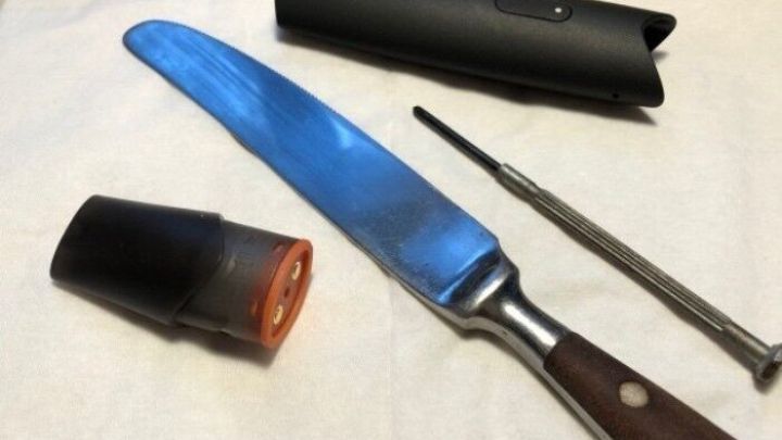 Eine gro&szlig;e Klinge liegt neben einem E-Zigaretten-Cap und Werkzeug, w&auml;hrend alles auf einem hellen Untergrund platziert ist.