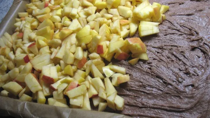 Der Teig wird gleichm&auml;&szlig;ig auf dem mit Backpapier ausgelegten Blech und dar&uuml;ber die Apfelst&uuml;ckchen und Rosinen verteilt.  