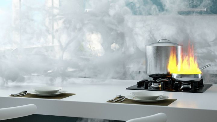 Ein Pfannenobjekt bruzelt auf dem Herd, w&auml;hrend Rauch und Flammen in einer modernen K&uuml;che aufsteigen.