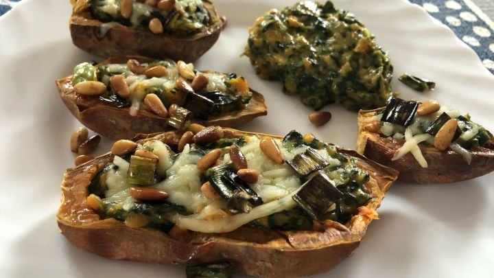 Gef&uuml;llte S&uuml;&szlig;kartoffeln liegen auf einem wei&szlig;en Teller, gef&uuml;llt mit Spinat und K&auml;se, umgeben von einem bunten Untergrund.