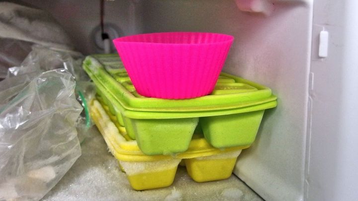 Eine pinke Muffinform steht auf gr&uuml;nen und gelben Eisw&uuml;rfelschalen im Gefrierfach, bereit f&uuml;r das einfache L&ouml;sen von Muffins.