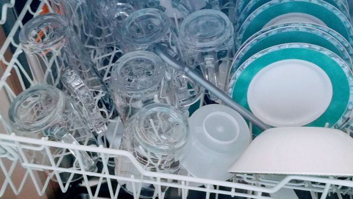 Eine Sp&uuml;lmaschine mit Gl&auml;sern und Tellern, die zum Reinigen gef&uuml;llt ist, steht in einer modernen K&uuml;che.