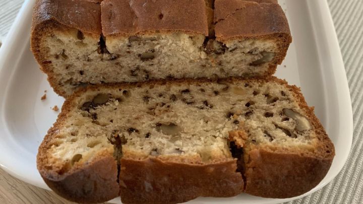 Ein frisch gebackener Nussbrotkuchen liegt auf einem wei&szlig;en Teller, einige St&uuml;cke sind bereits abgeschnitten und zeigen die nussige F&uuml;llung.