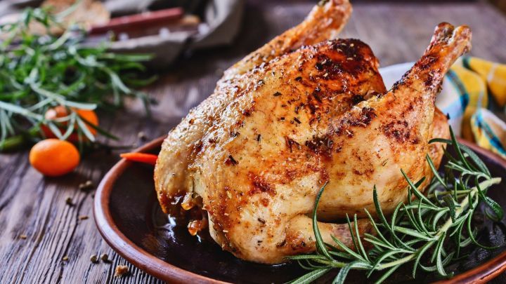 Ein knuspriges H&auml;hnchen liegt auf einem rustikalen Tisch, umgeben von frischen Kr&auml;utern und einer gem&uuml;tlichen Atmosph&auml;re.