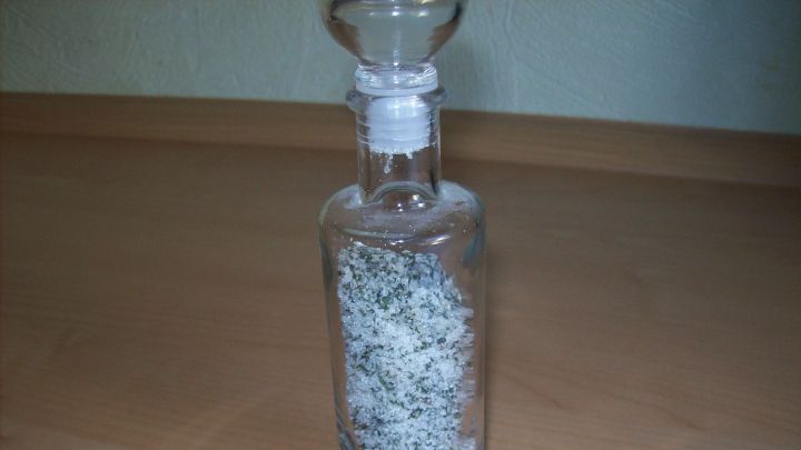 In einer Glasflasche befindet sich Zucker, gemischt mit Minze, auf einem Tisch in einer einfachen Umgebung.